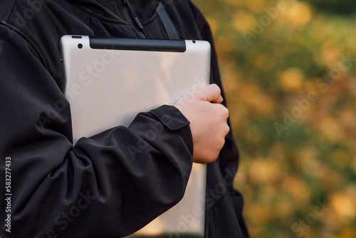 horizontal photo close-up boy with tablet near school with online learning book, tablet in child's hands,hold the tablet close to your body, schoolgirl, on beautiful yellow-green background, blurred