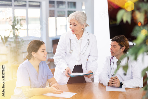 Group of professional doctors of different ages sitting at table and discussing diagnosis and treatment of patients during medical council