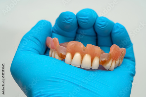 A man's hand in a rubber blue glove holds a denture. Close up.