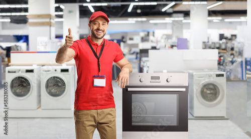 Salesman with electrical appliances leaning on an oven in a store and gesturing thumbs up