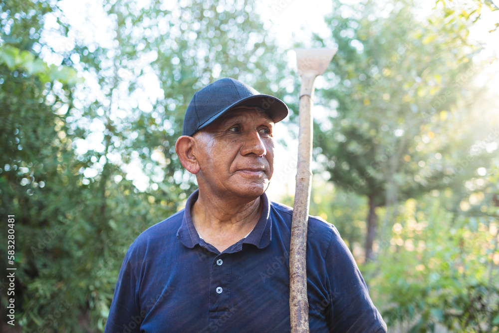 Obraz premium Headshot portrait of a senior indigenous mapuche farmer man holding a garden scraper in countryside