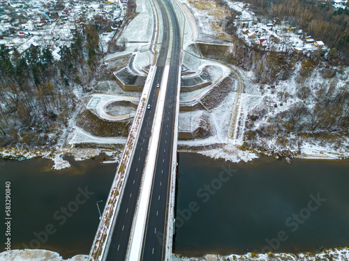Top view of the roadway in winter. Snow-covered road and roadside. The highway passes through the forest and the private sector. Detailed photos from the drone of the road infrastructure.