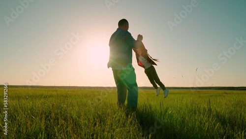 Happy family father child play, park sun. Dad twists his daughter holding hands. Fun family concept, childhood dream to fly. Cheerful people in park. Happy dad, child daughter circling on green meadow