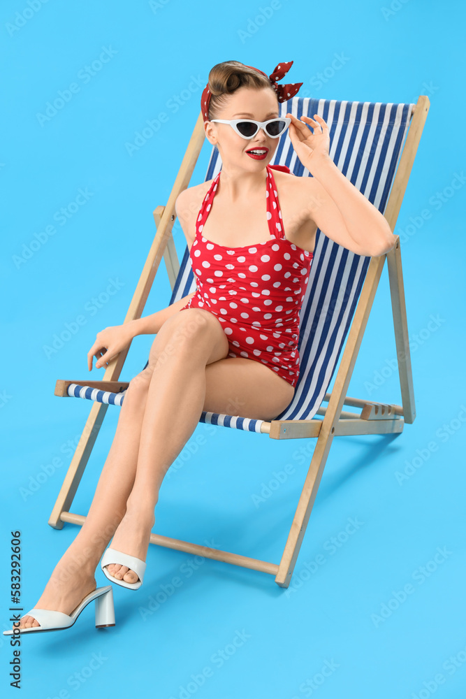 Young pin-up woman sitting in deck chair on blue background Young pin-up woman sitting in deck chair on blue background