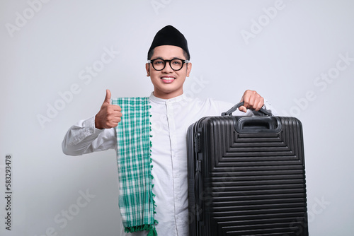 Asian muslim man showing thumb up sign while holding a black suitcase. photo