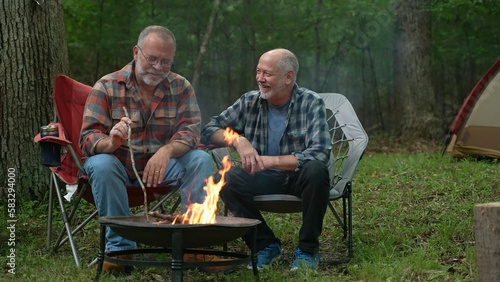 Closeup of two gay men in front of campfire laughing and smiling celebrating pride.
