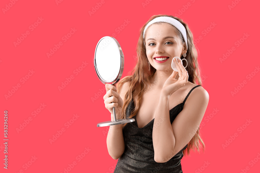 Young woman with mirror removing makeup on red background Young woman with mirror removing makeup on red background