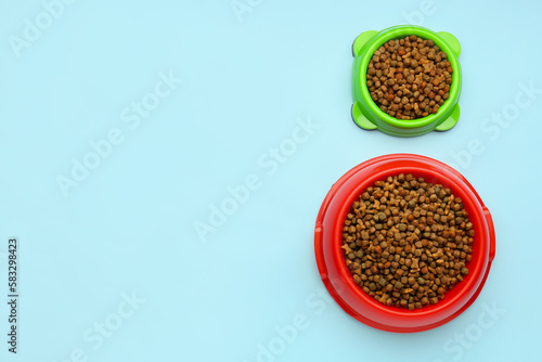 Bowls of dry pet food on color background