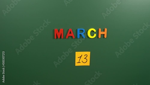Hand sticking a sticker 13 March calendar day on school board. 13 date of March. Thirteenth day of March. 13th date number. 13 day calendar. Thirteen date. Daylight Saving Time photo