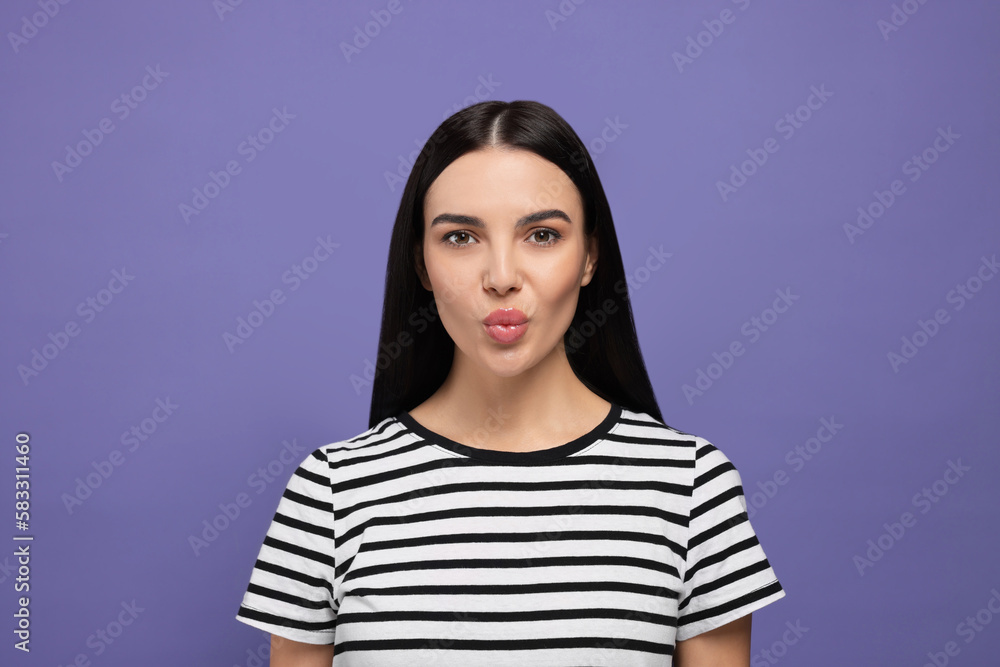 Fototapeta premium Beautiful young woman blowing kiss on purple background