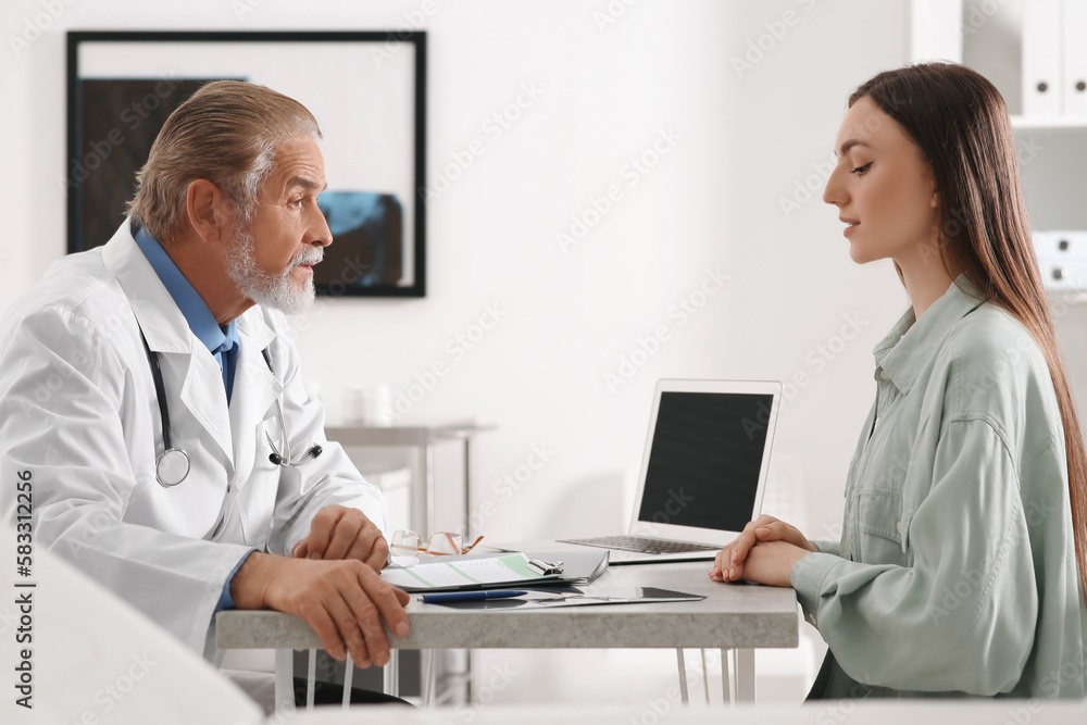 Professional orthopedist consulting patient at table in clinic Professional orthopedist consulting patient at table in clinic