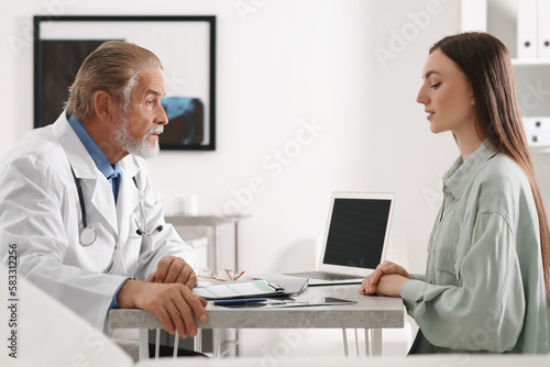 Professional orthopedist consulting patient at table in clinic
