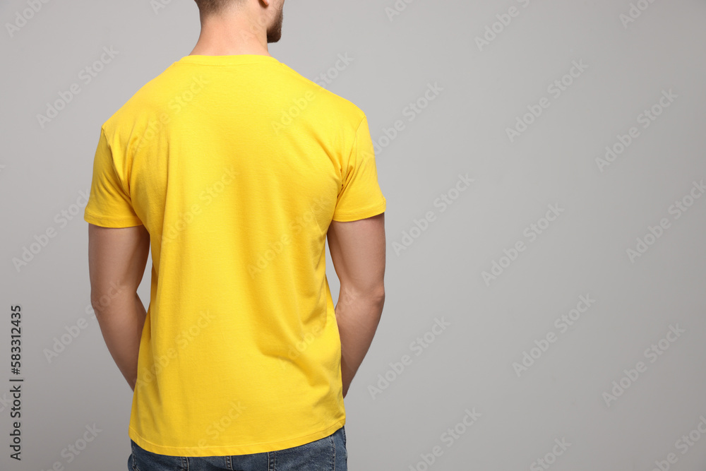 Man wearing yellow t-shirt on light grey background, back view. Mockup ...
