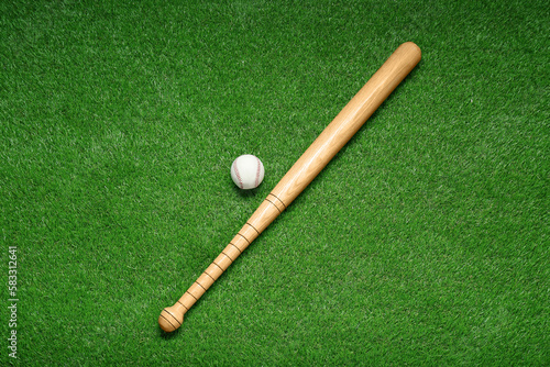 Wooden baseball bat and ball on green grass, flat lay. Sports equipment