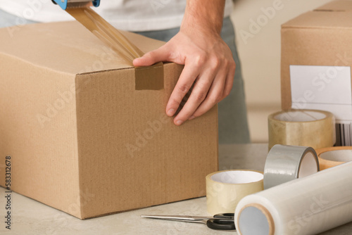 Fotografi Man packing box with adhesive tape indoors, closeup