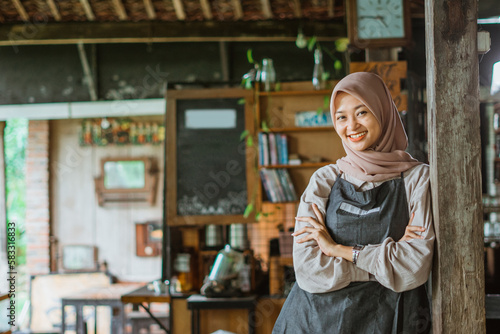 muslim female barista standing with handcrossed leaning on the wood pillar inside the cafe