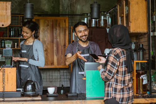 the male barista pointing on the board with green screen while giving service to the customer at the coffee shop