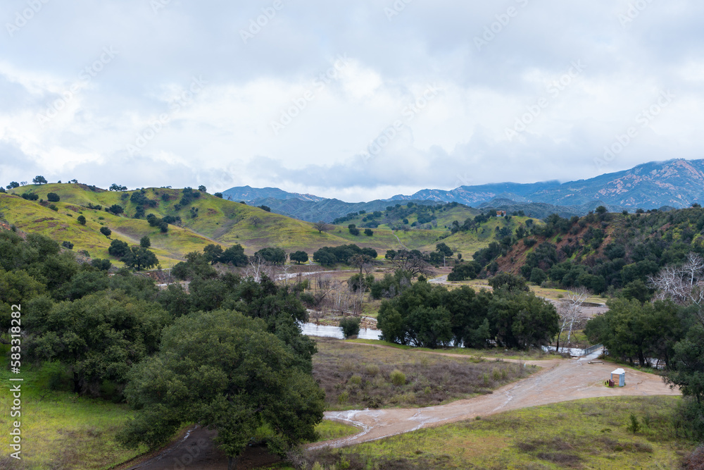 Malibu Creek State Park muddy after a large rainfall in southern California. Streams overflowing, lush green grass, large oak trees, clouds, dam rushing, water flowing.