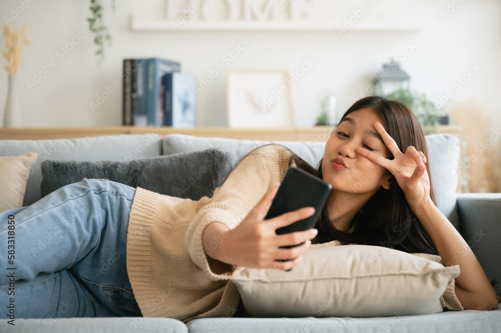 Happy young asian woman relax on comfortable couch at home texting messaging on smartphone, smiling girl use cellphone, browse wireless internet on gadget, shopping online from home Happy young asian woman relax on comfortable couch at home texting messaging on smartphone, smiling girl use cellphone, browse wireless internet on gadget, shopping online from home