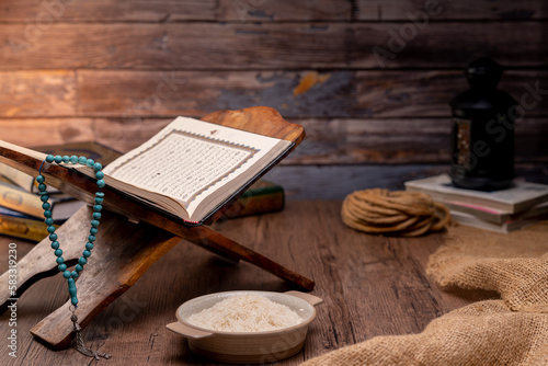 Holy Quran and a grain of rice in a wooden bowl in the sack on a wooden table, Islamic zakat concept. Muslims help the poor and needy. Conceptual shoot for property, income, and fitrah zakat.