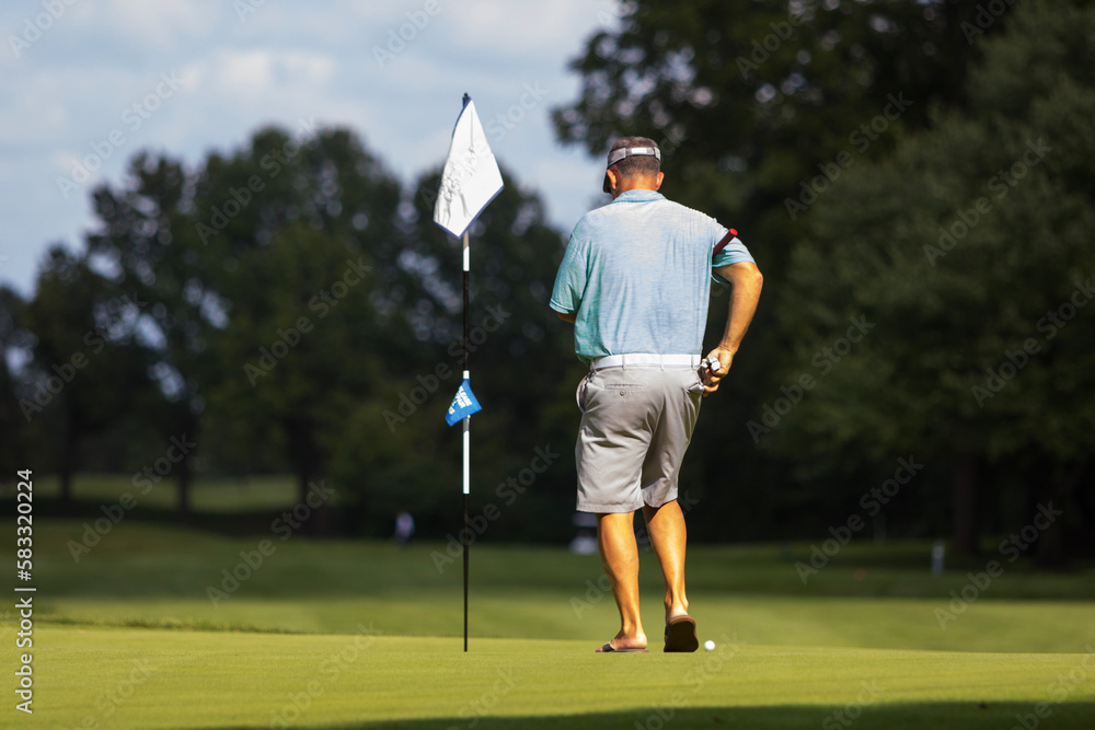 A male golfer walking towards a golf flag on the course with green grass underneath him.