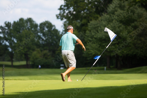 A male golfer walking towards a golf flag on the course with green grass underneath him.