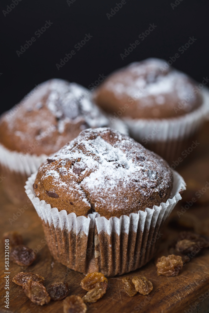 Close up of fresh muffins with chocolate on a wooden board with dry grapes