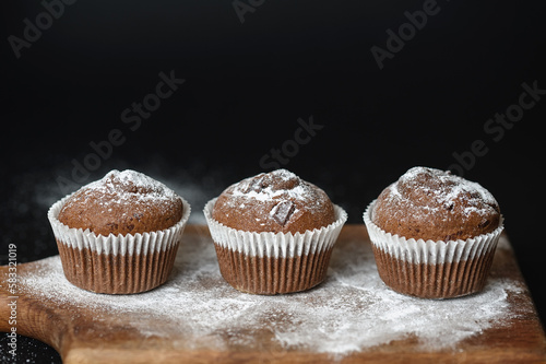 Fresh muffins with chocolate on a wooden board