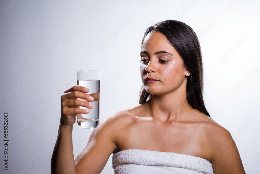 Fototapeta premium A beautiful young woman takes a moment to hydrate with water before going to bed. Shot in a studio on a white background, her natural beauty radiates.