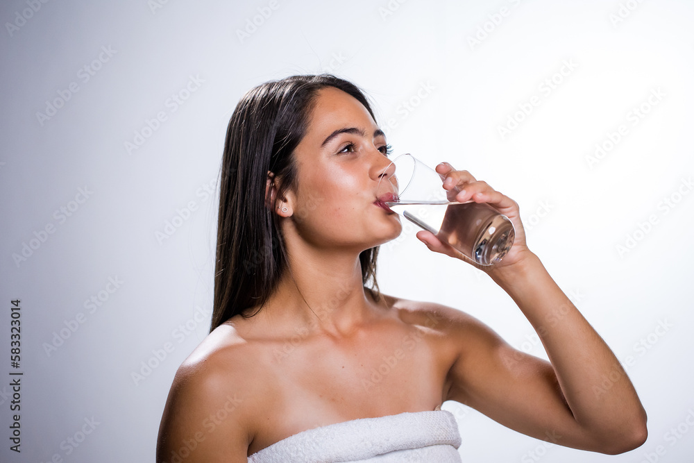 A beautiful young woman takes a moment to hydrate with water before going to bed. Shot in a studio on a white background, her natural beauty radiates. A beautiful young woman takes a moment to hydrate with water before going to bed. Shot in a studio on a white background, her natural beauty radiates.