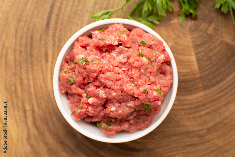 Raw Ground Beef in White Bowl on Wooden Board from Above Raw Ground Beef in White Bowl on Wooden Board from Above