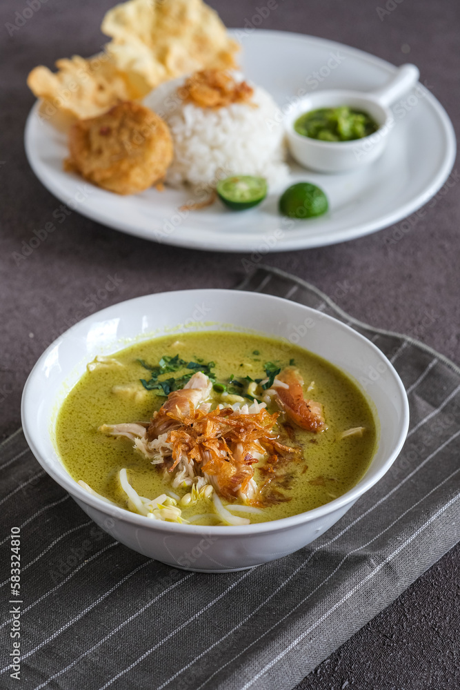 soto ayam or chicken yellow soup in white ceramic bowl, usually served with cooked rice, and potatoes cake