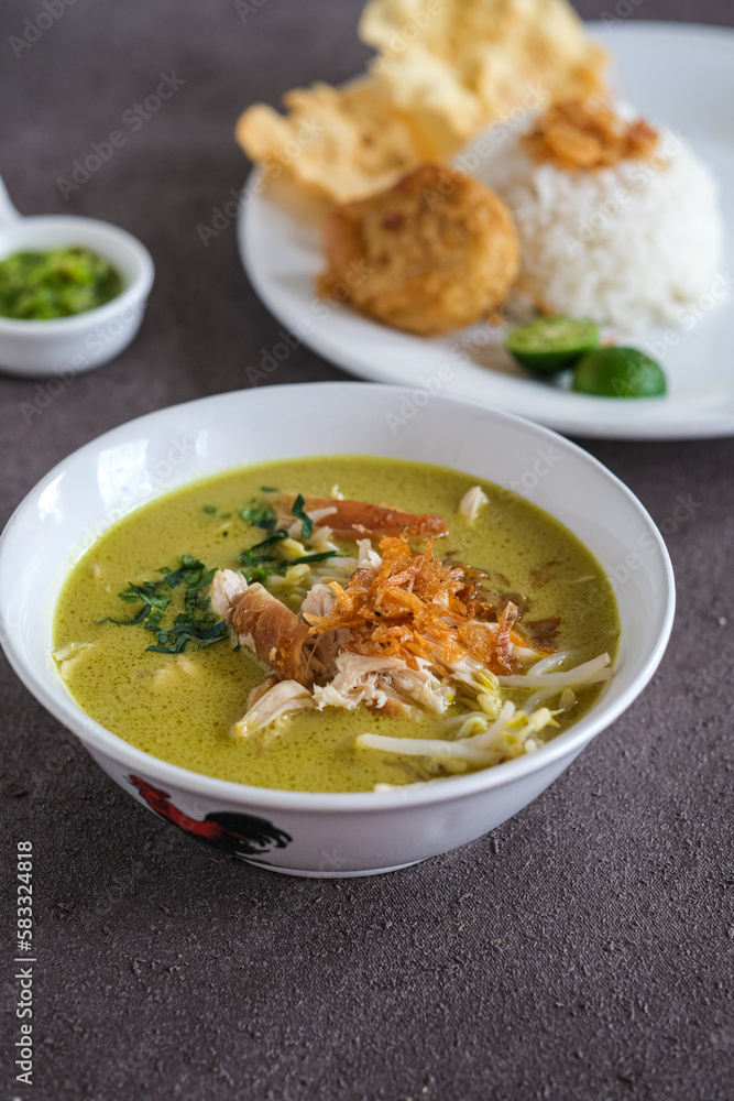 soto ayam or chicken yellow soup in white ceramic bowl, usually served with cooked rice, and potatoes cake soto ayam or chicken yellow soup in white ceramic bowl, usually served with cooked rice, and potatoes cake