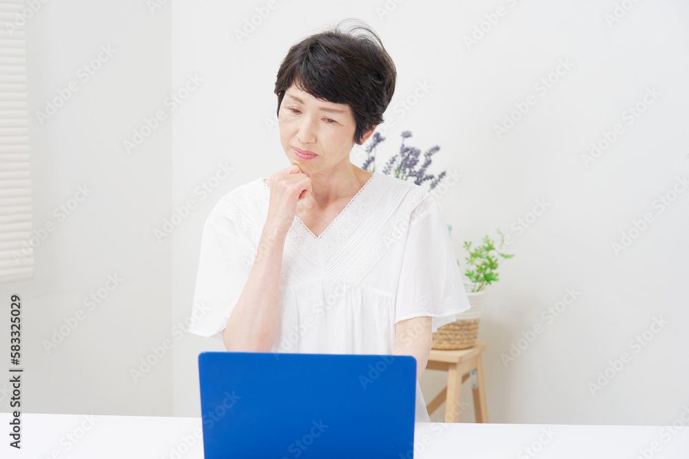 家でノートパソコンを見て考える中年女性