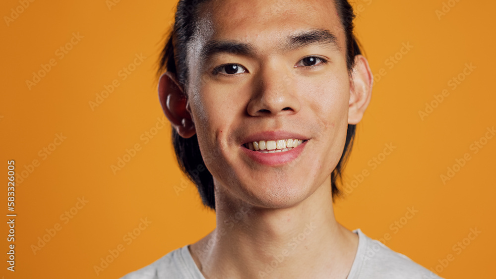 Happy man smiling and being excited on camera, posing over orange background with confidence. Young asian model acting positive and friendly in studio, hipster with athletic casual style. Happy man smiling and being excited on camera, posing over orange background with confidence. Young asian model acting positive and friendly in studio, hipster with athletic casual style.
