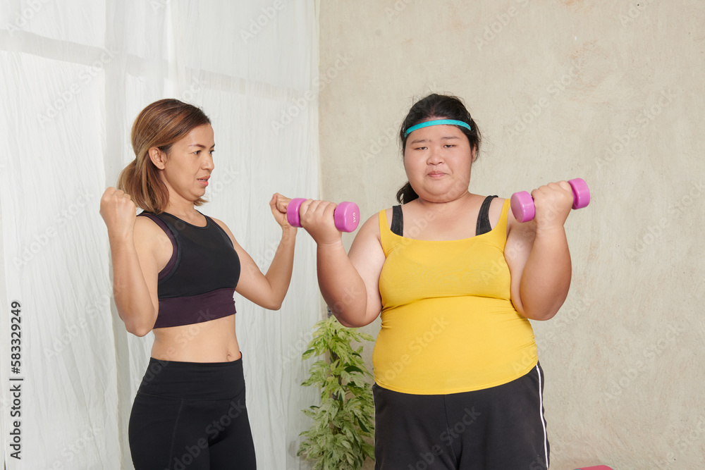 Tired exhausted young asian fat woman weights workout at home in living room. professional fitness female trainer giving personal training to overweight young woman, intend to exercise for health. Tired exhausted young asian fat woman weights workout at home in living room. professional fitness female trainer giving personal training to overweight young woman, intend to exercise for health.