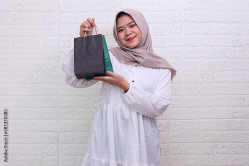 Cheerful beautiful Asian muslim woman wearing hijab showing little shopping bags and looking at camera. 