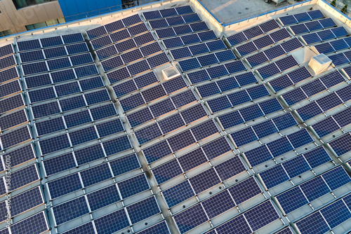 Aerial view of solar power plant with blue photovoltaic panels mounted on industrial building roof for producing green ecological electricity. Production of sustainable energy concept