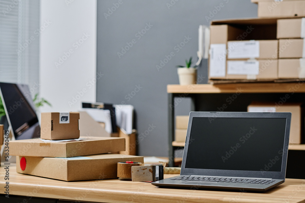 Laptop and stack of cardboard packed boxes with clothes standing on workplace of volunteer in storage room or office of organization Laptop and stack of cardboard packed boxes with clothes standing on workplace of volunteer in storage room or office of organization