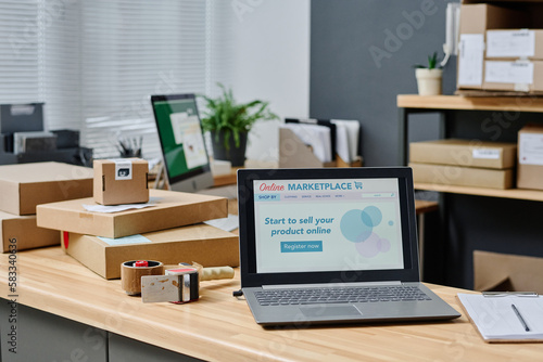 Workplace of volunteer with homepage of online marketplace on laptop screen, stack of packed boxes with clothes for people in need