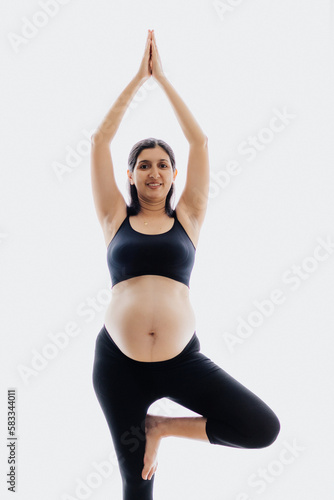 Pregnant beautiful blonde woman is wearing sportive black clothes doing yoga exercises isolated, healthy life concept
