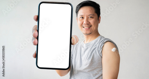 Man holding down him shirt sleeve and showing him arm with bandage after receiving accination, holding a large smartphone with a blank screen. photo