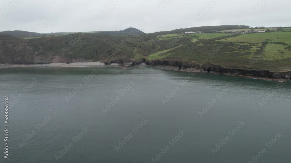 Coast with rugged rocks and wooded slope. Forwards fly above calm sea surface near shore. Amroth, South Wales, UK Coast with rugged rocks and wooded slope. Forwards fly above calm sea surface near shore. Amroth, South Wales, UK