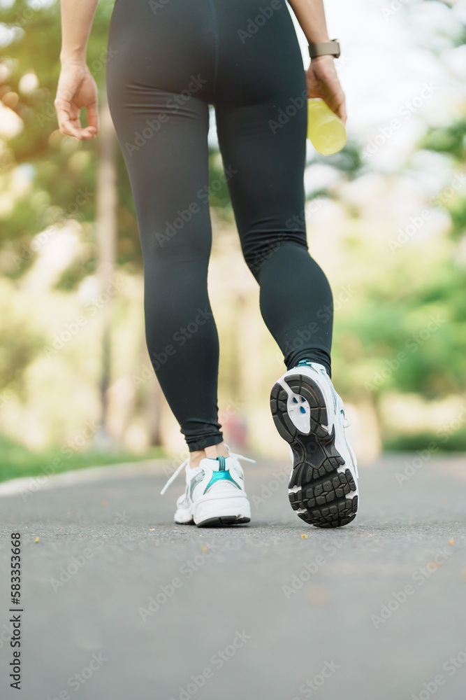 woman jogging and walking on the road at morning, Young adult female in sport shoes running in the park outside, leg muscles of Athlete. Exercise, wellness, healthy lifestyle and workout concepts