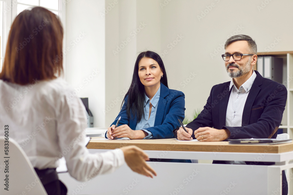 Young brunette woman at interview and two business partners listening attentively to their potentially new employee. Three people at meeting in bright modern office. Candidate for position in company. Young brunette woman at interview and two business partners listening attentively to their potentially new employee. Three people at meeting in bright modern office. Candidate for position in company.