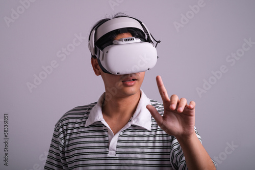 Surprised teen male student use vr glasses and looks at empty space with gray background. Virtual gadgets for entertainment, work, free time and study. Virtual reality metaverse technology concept. © Bordinthorn