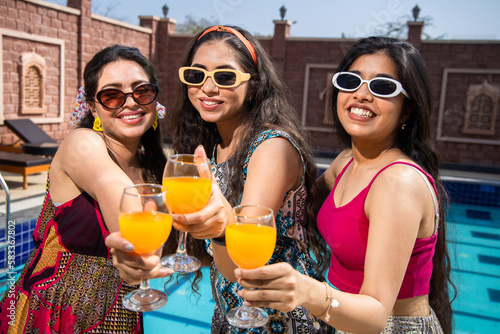 Photography Three beautiful young indian girls wearing sunglasses having fun together holding glasses of drinks cocktail in hot summer day at resort
