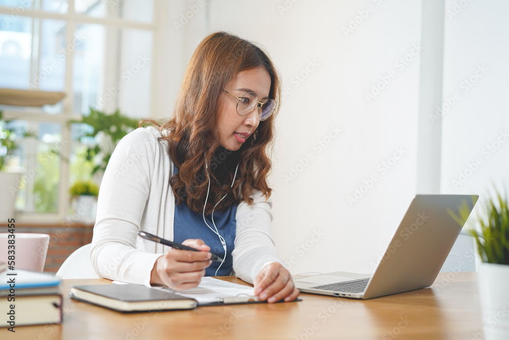 Asian people study online course via internet. Young girl watching business lesson from laptop computer and note lecture to notebook at home. Asian people study online course via internet. Young girl watching business lesson from laptop computer and note lecture to notebook at home.