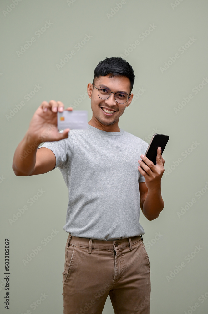 Happy Asian man holding his smartphone and showing a credit card to camera Happy Asian man holding his smartphone and showing a credit card to camera