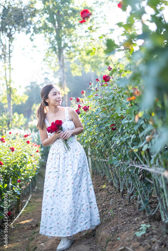 Young Asian woman wearing a white dress poses with a rose in rose garden, Chiang Mai Thailand
